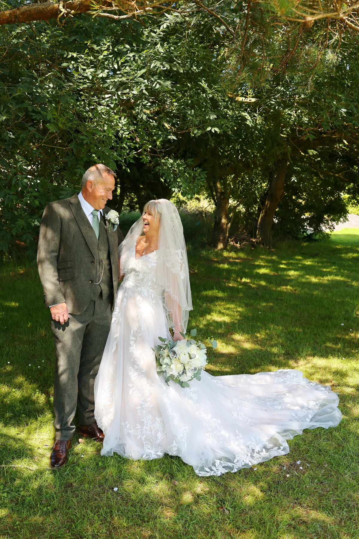 A bride and her father under the trees in the grounds