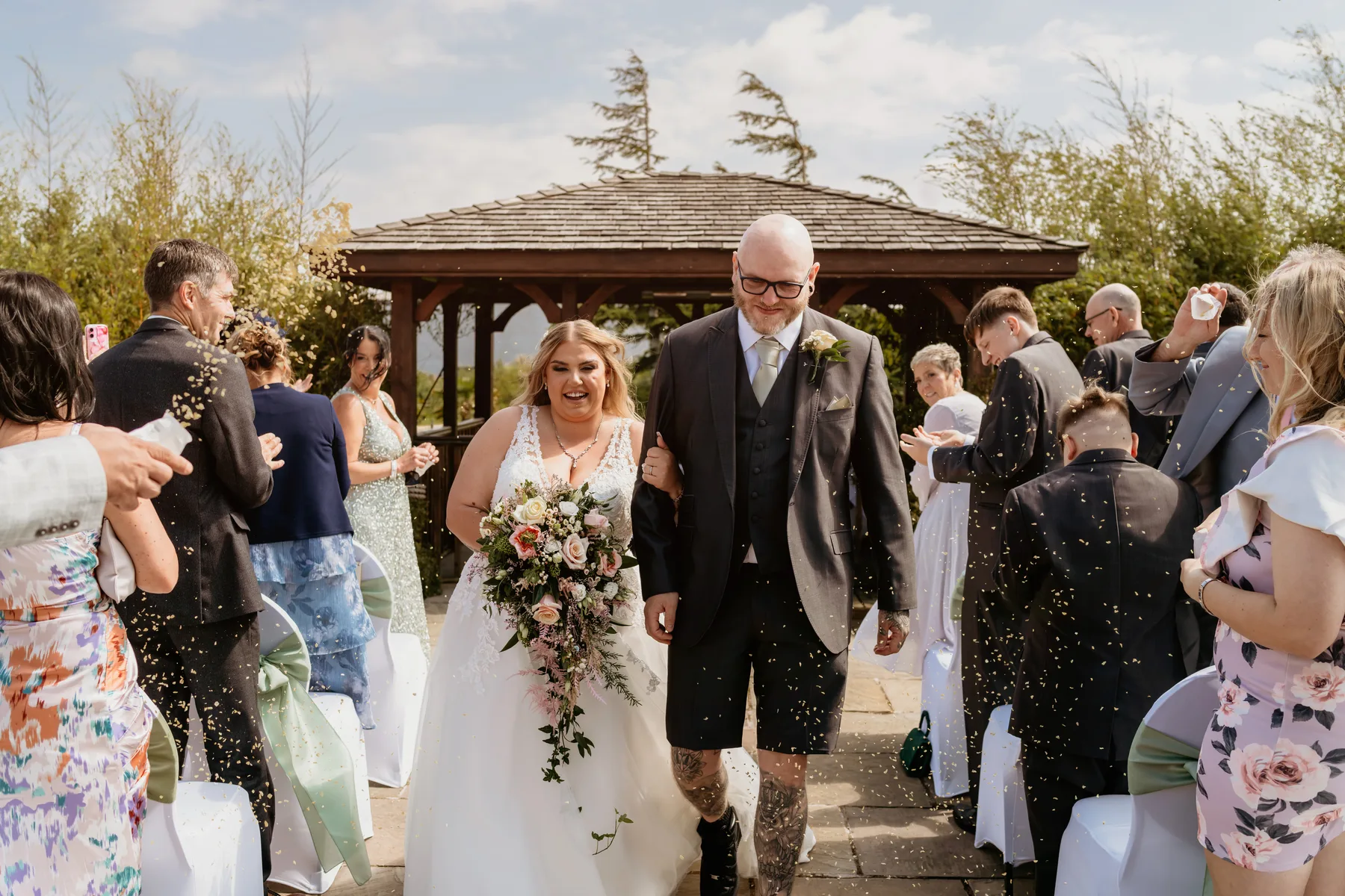 A couple walking back through confetti after their ceremony, the gazebo behind them