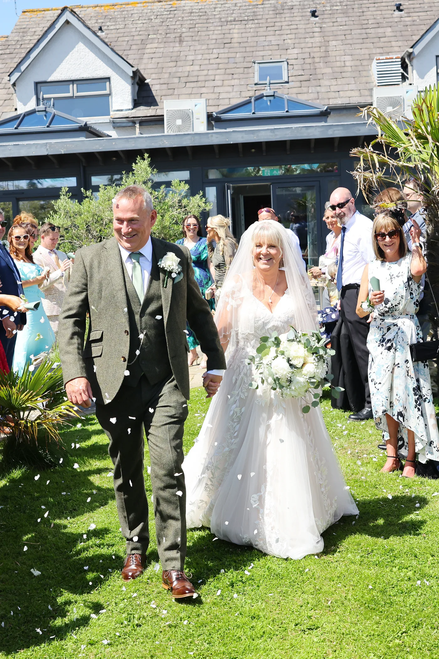 A newly married couple walking through confetti on the lawns